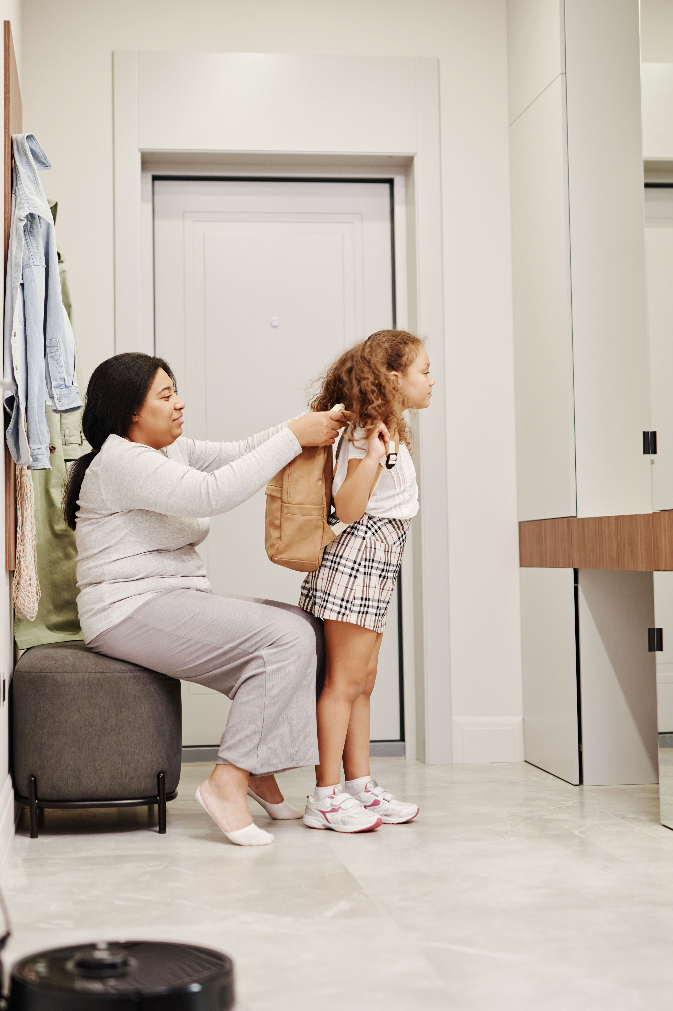 Mother helping daughter with backpack at home